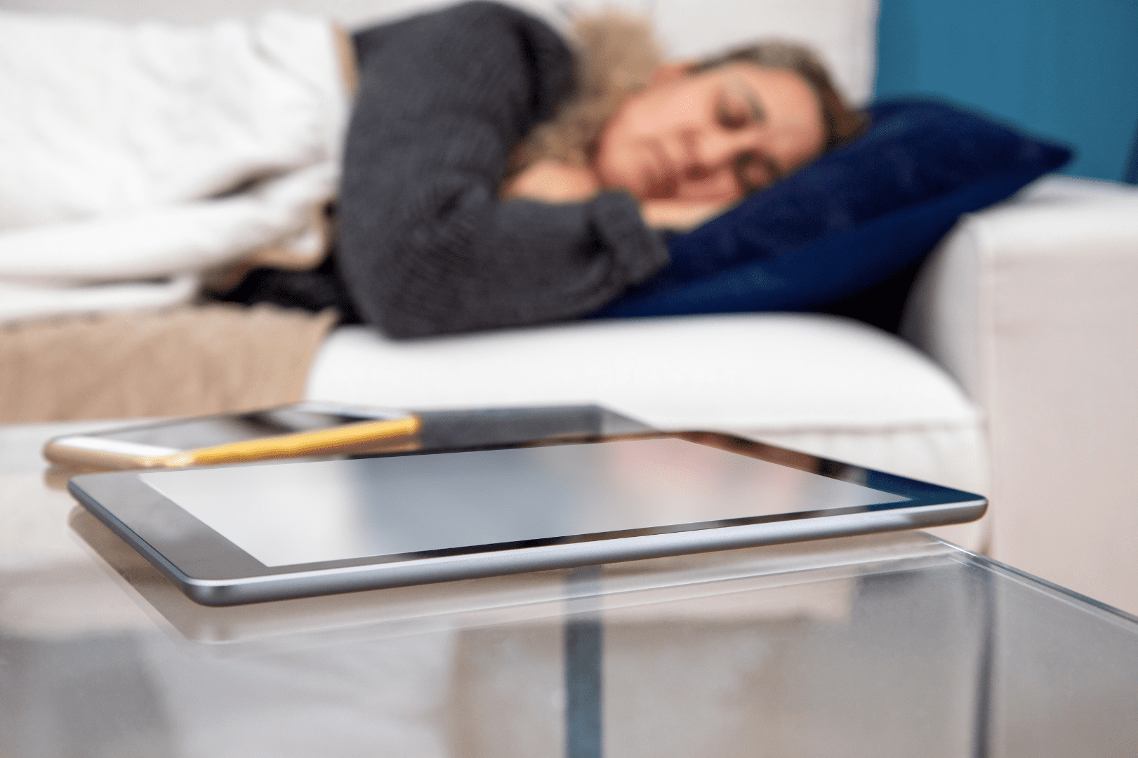 Illustration de l'hyperconnectivité. Personne dormant sur un canapé. Un téléphone mobile et une tablette sont visibles en avant-plan.